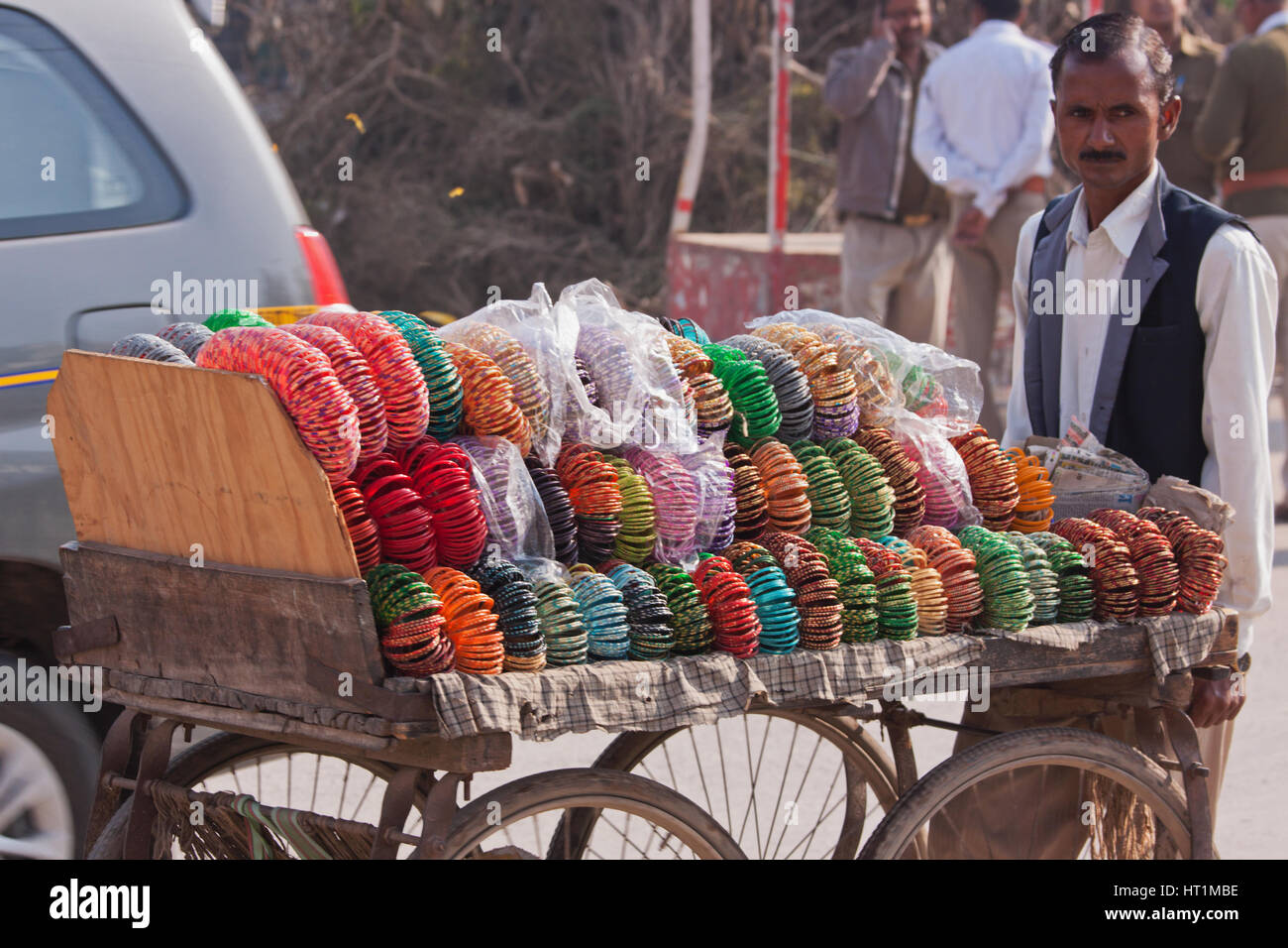 Un commerciante non identificato ruote il suo barrow di coloratissimi bracciali e anelli di testa per la vendita per il vicino Passo di strada di Varanasi, India Foto Stock