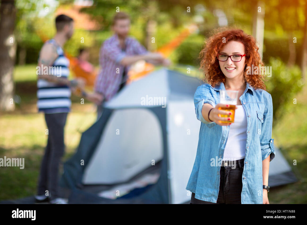 Curly redhead donna offre un bicchiere di birra in foresta Foto Stock