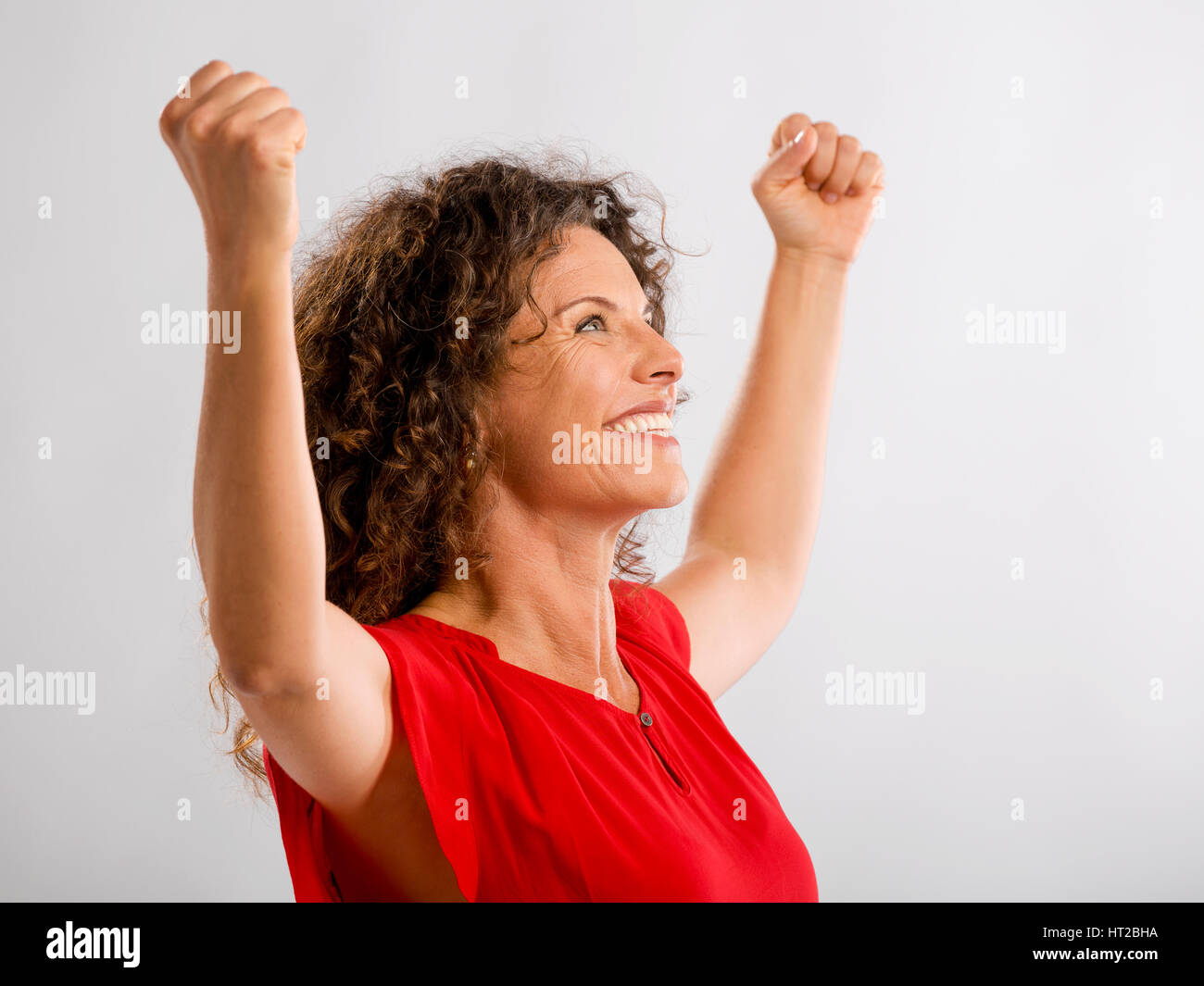 Ritratto di un felice di mezza età brunette con le braccia in alto che esprimono la vittoria Foto Stock