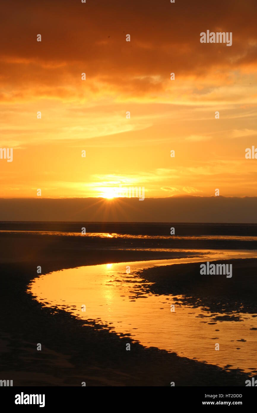 Impostazione di sole su una spiaggia di sabbia con un movimento serpeggiante fiume nella massa anteriore Foto Stock