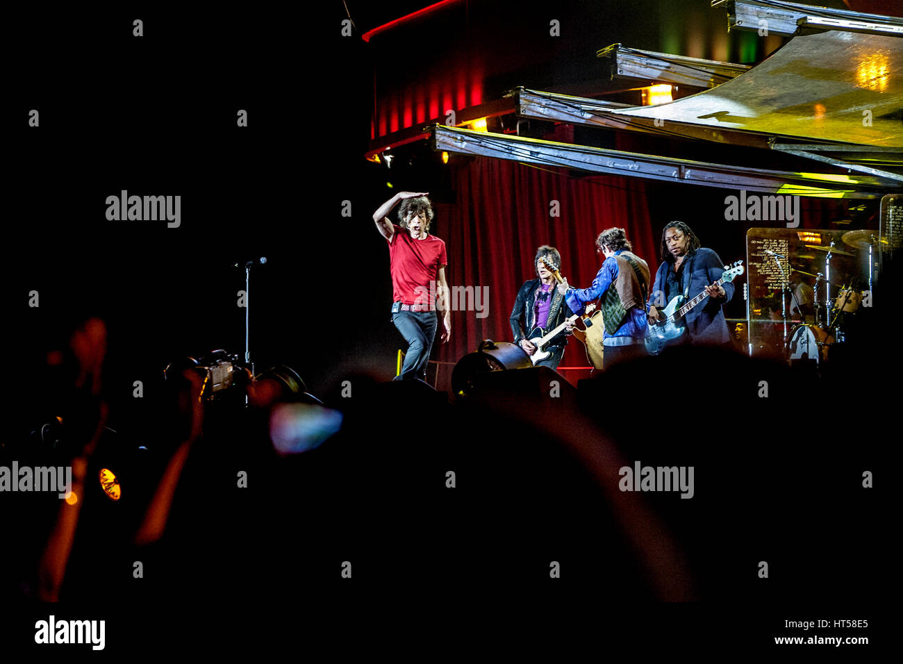 Mick Jagger ombreggiatura i suoi occhi dai riflettori guardando il pubblico sul palco a suonare la chitarra in Rolling Stones Foto Stock