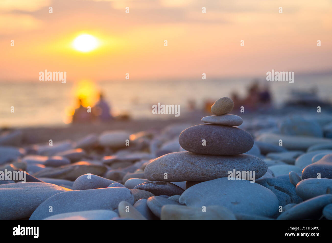 Un giovane e ripiegati a piramide Zen pietre ghiaia sul mare spiaggia al tramonto Foto Stock