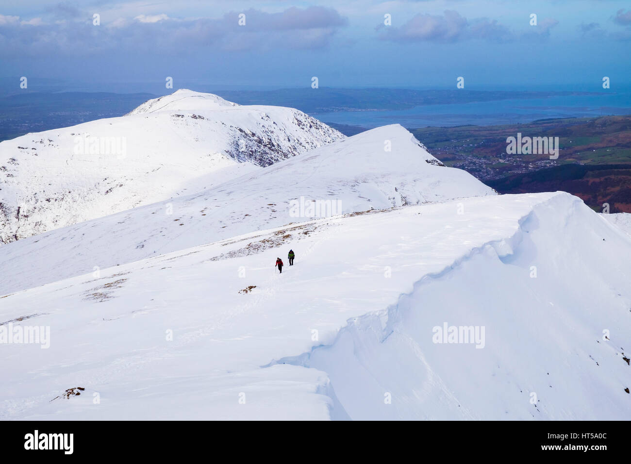 Vista da Y Garn montagna a nord Glyderau gamma nel Parco Nazionale di Snowdonia montagne con gli escursionisti escursionismo in inverno la neve e la costa al di là. Wales UK Foto Stock