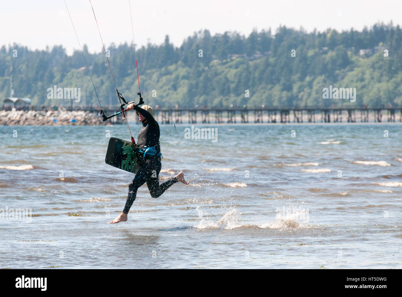 Uomo che corre nel surf su una spiaggia kitesurf con scheda nella mano che indossa una muta umida. Foto Stock