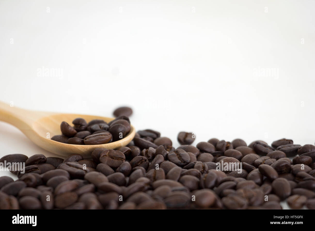 Chicchi di caffè tostati e un cucchiaio di legno su sfondo bianco Foto Stock