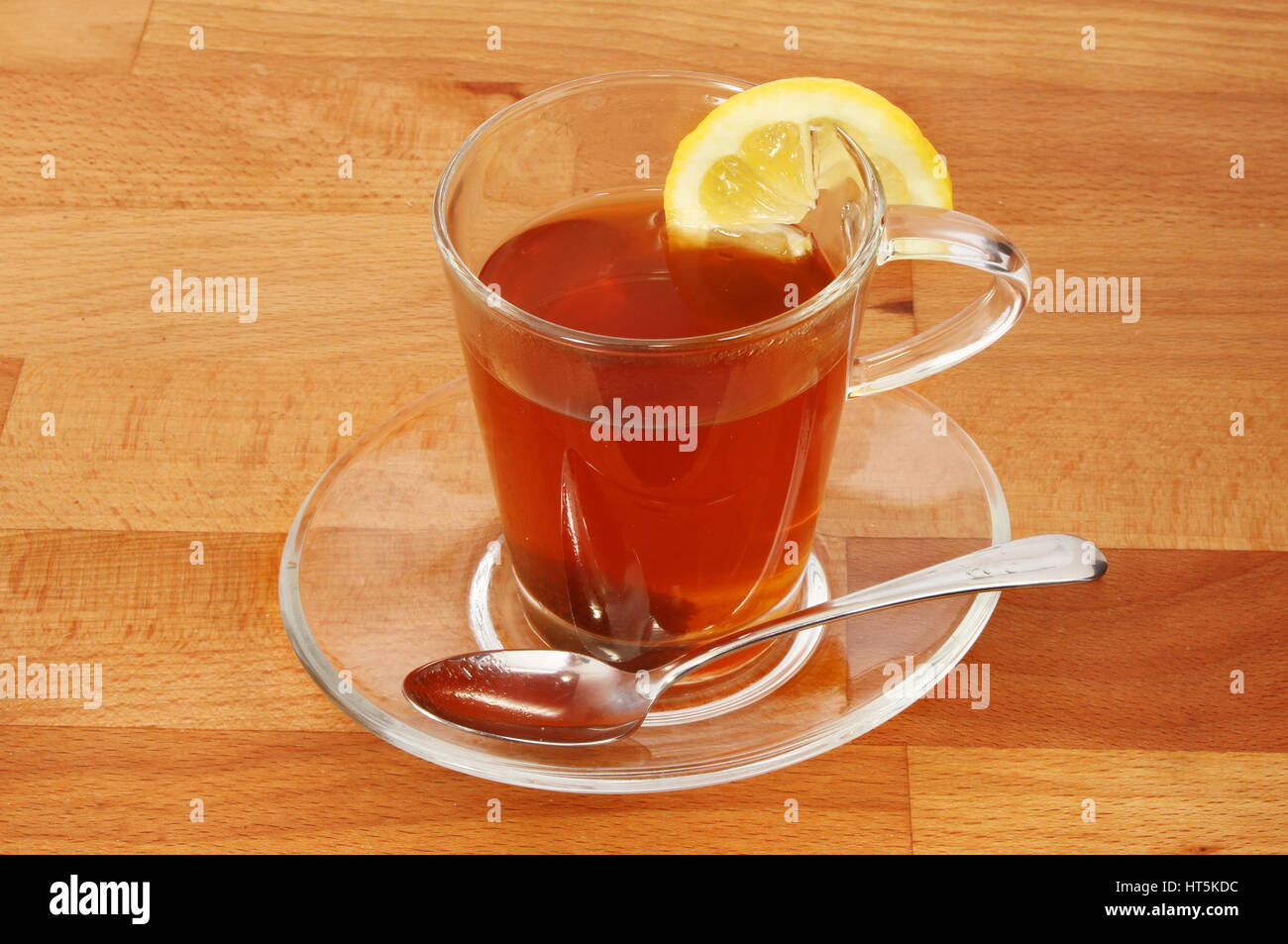 Tè al limone in un bicchiere di vetro e il piattino su un piano di lavoro in legno Foto Stock