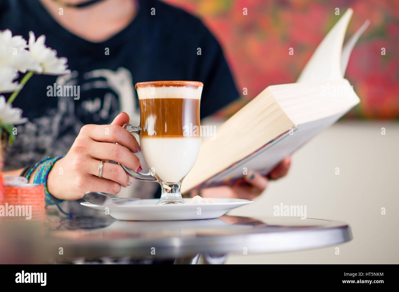 Ragazza di bere il cappuccino all'interno di un Art cafe durante la lettura di un libro Foto Stock
