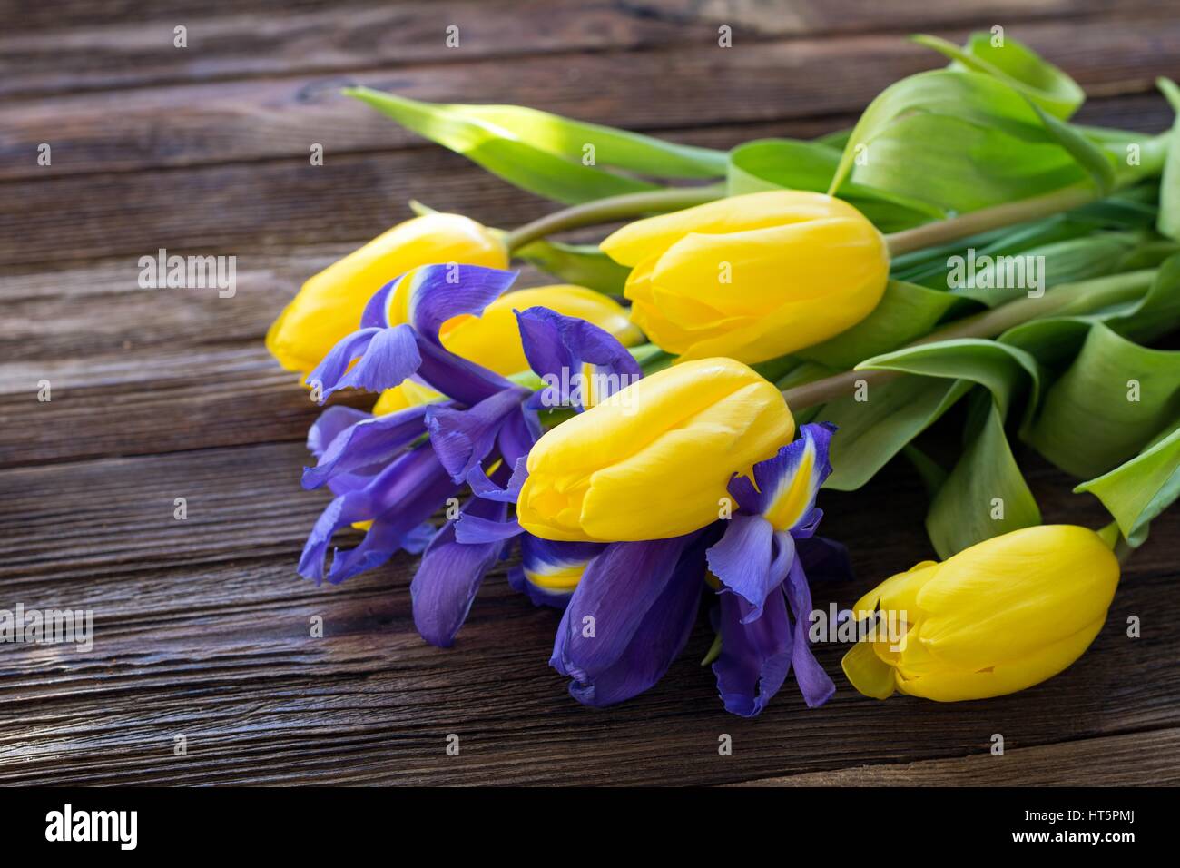 Bouquet di tulipani gialli e iride fiori su un tavolo di legno, raggi di luce del sole colpisce sullo sfondo. Primo piano. Womens giorno, madri giorno concept Foto Stock