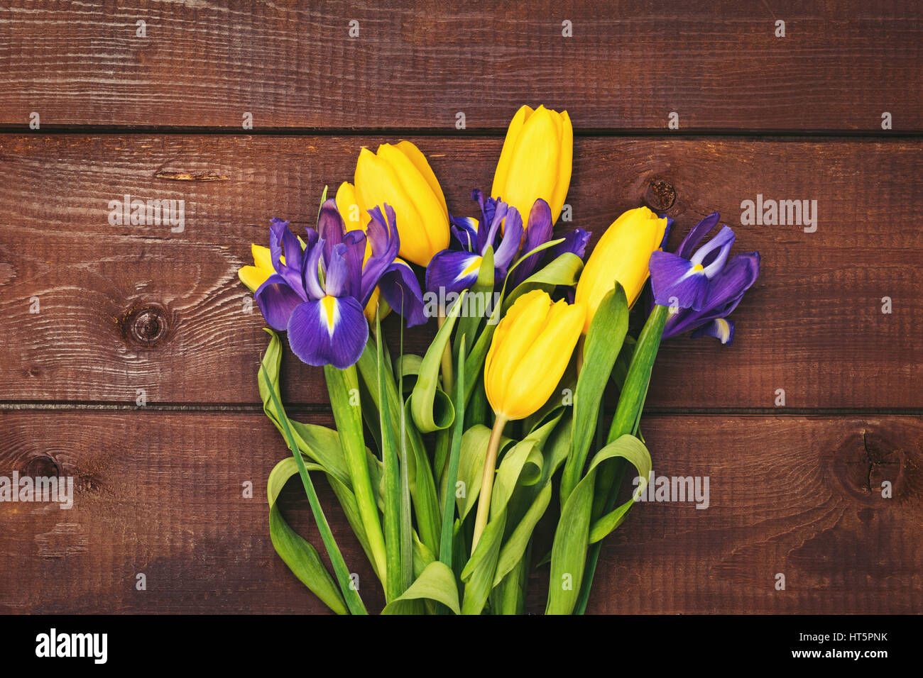 Bouquet di fiori. Tulipani gialli e iride fiori su legno marrone dello sfondo. Tabella vista superiore e copia spazio per il testo. Fiori di pasqua Foto Stock