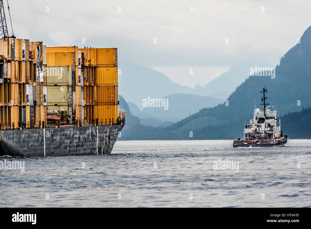 In un giorno nuvoloso, una direzione sud rimorchiatore tira una chiatta caricato con contenitori lungo Johnstone Strait, parte della British Columbia passaggio interno. Foto Stock