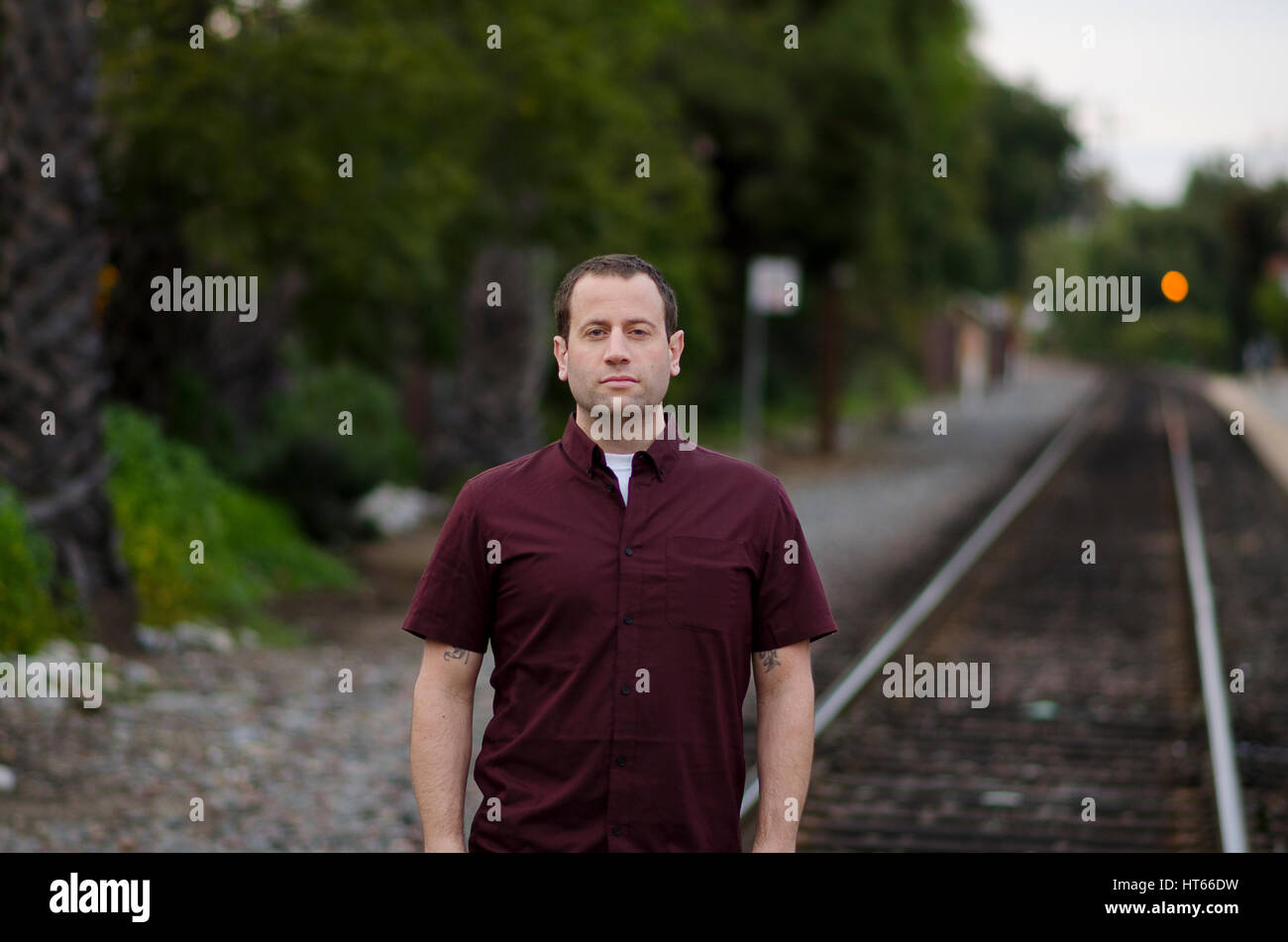 Uomo con una grave espressione di poppa in piedi sui binari della ferrovia da soli. Foto Stock