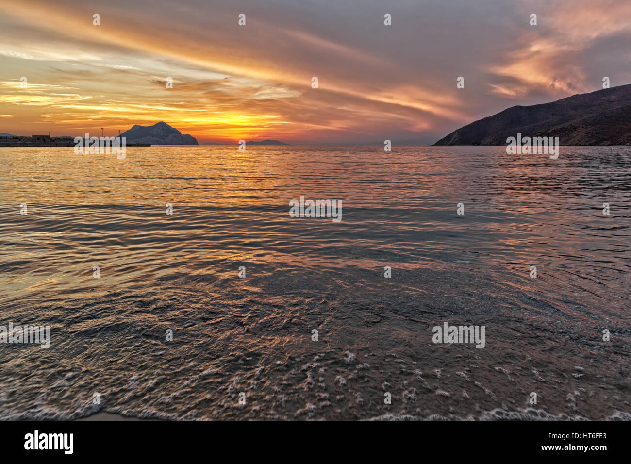 Tramonto sulla spiaggia con belle drammatico giallo e arancione del cielo. Silhouette di un'isola molto più avanti in vista. Foto Stock