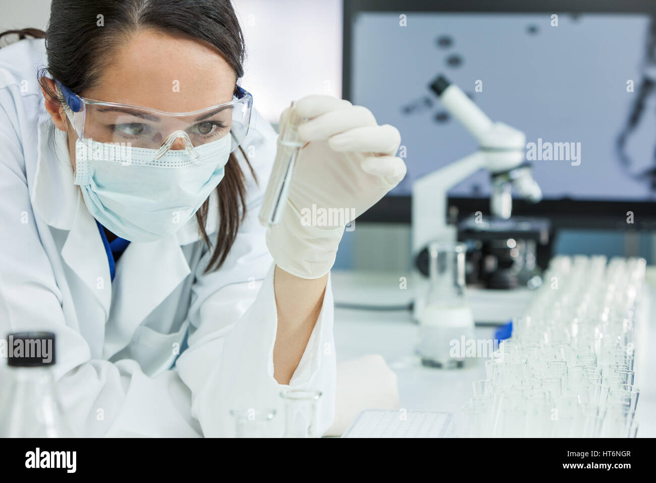 Una femmina la ricerca medica scienziato o donna dottore guardando un tubo di prova di una soluzione chiara in un laboratorio con il suo microscopio accanto a lei. Foto Stock