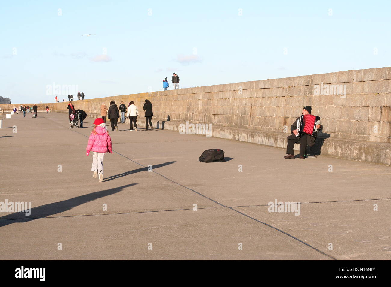 Howth Harbour, Dublino Irlanda. Bambina bambino camminando lungo la parete del porto, busker riproduzione di formare fisarmonica, vita migliore concetto, facile vivere, buona vita Foto Stock