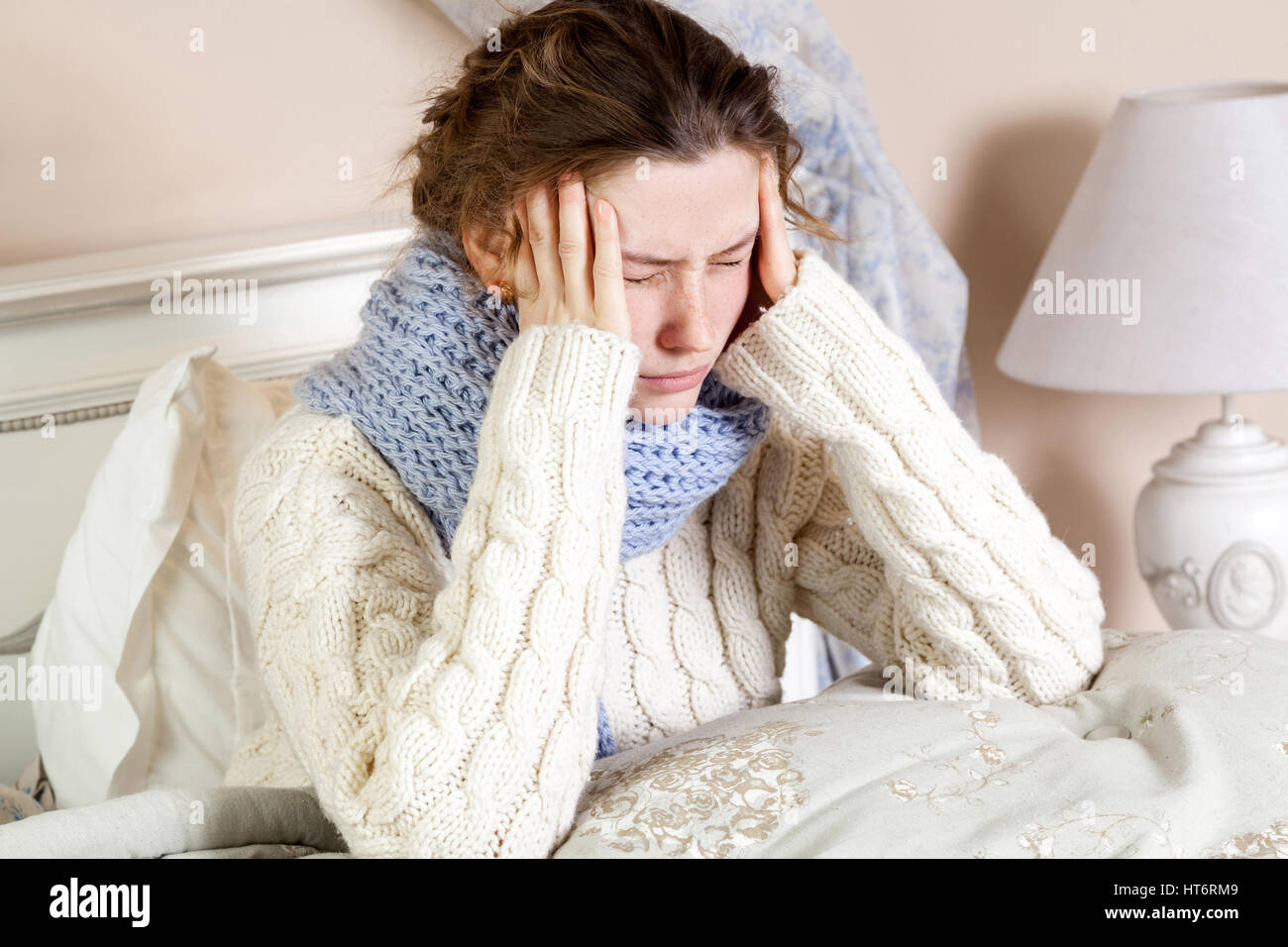 Influenza o freddo. Primo piano top visualizza immagine del frustrato giovane donna con sciarpa blu e soffre di terribili mal di testa mentre giaceva a letto. Foto Stock