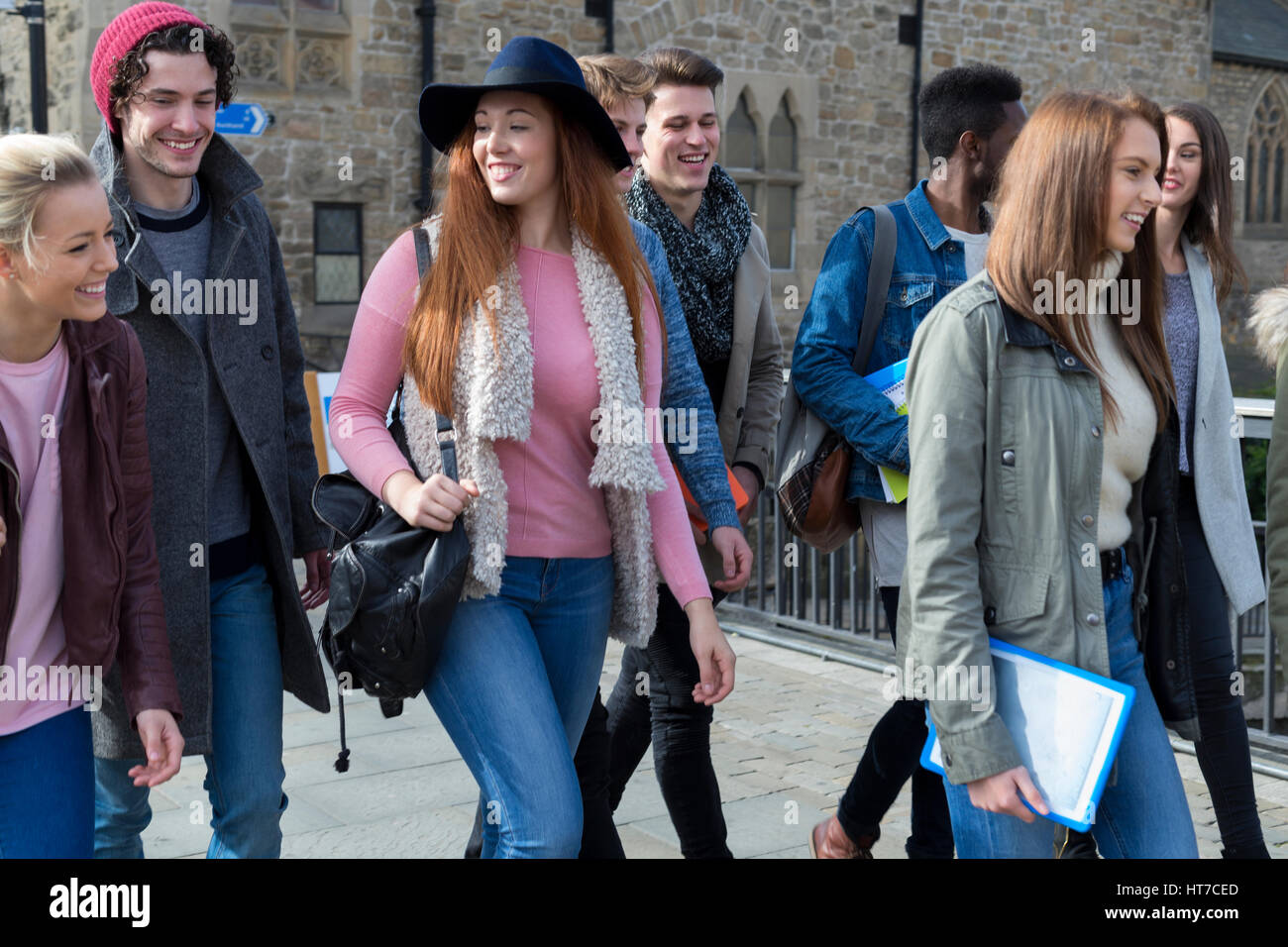 Un gruppo di felice giovani studenti sorriso a piedi attraverso la città insieme su una pausa dall'università. Essi stanno portando i loro sacchi, libri e cifre Foto Stock