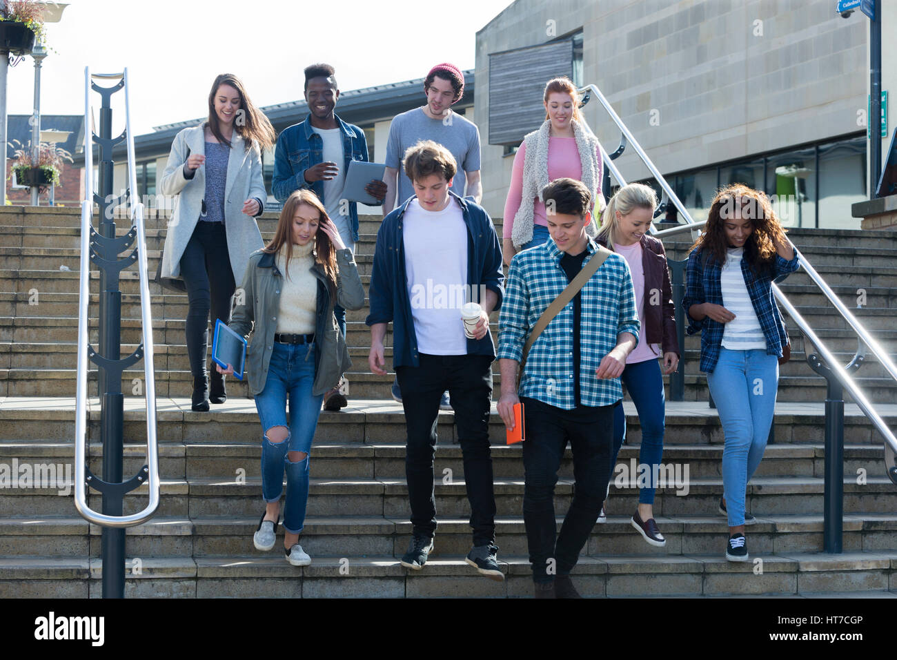 Un gruppo di giovani studenti adolescenti sorriso a piedi attraverso la città su di una pausa dall'università. Essi stanno portando i loro libri digitali e compresse. Foto Stock