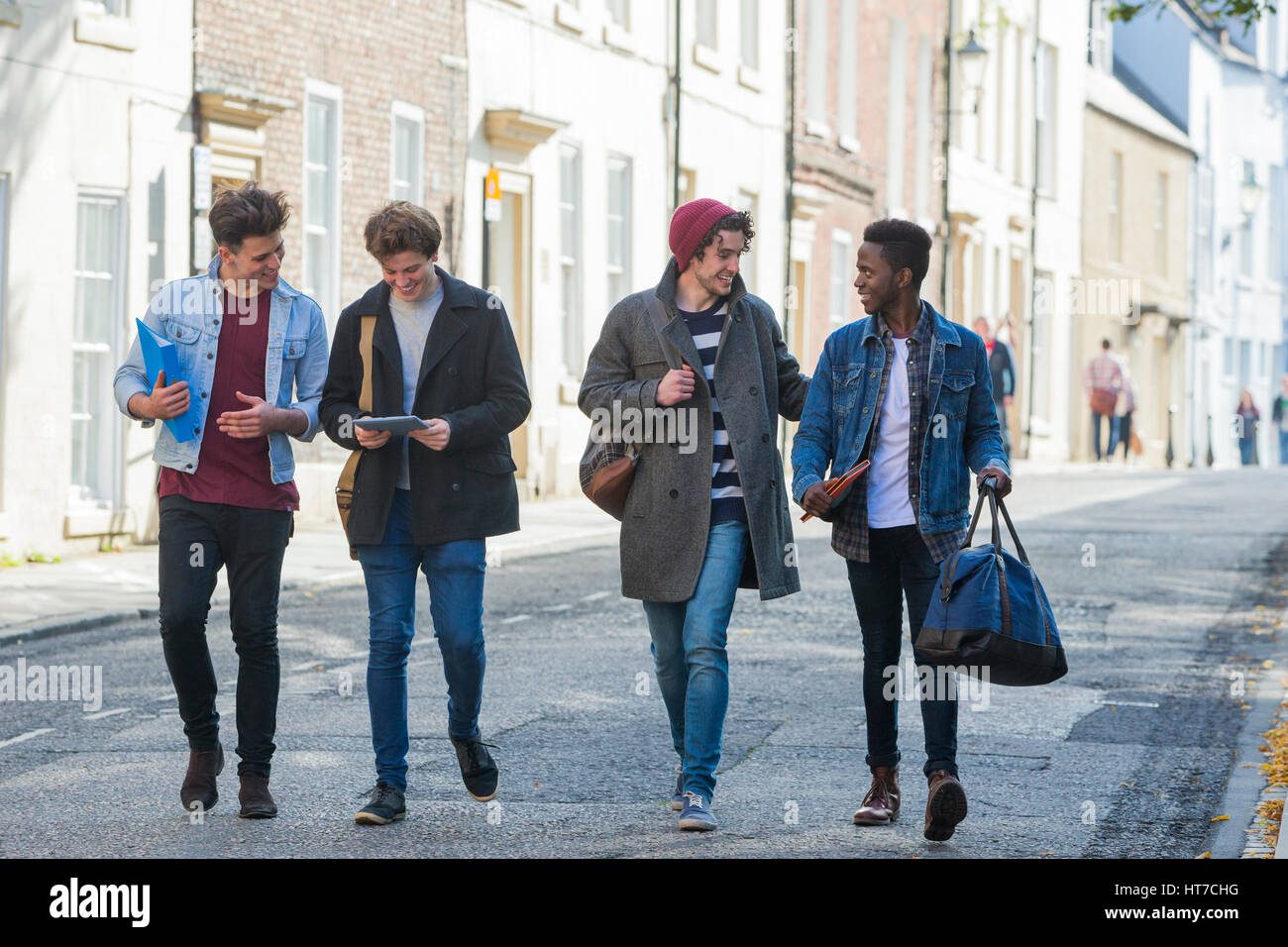 Un buon gruppo di studenti maschi sorridere e ridere come essi a piedi attraverso la città insieme. Essi stanno portando i loro sacchi e libri. Foto Stock
