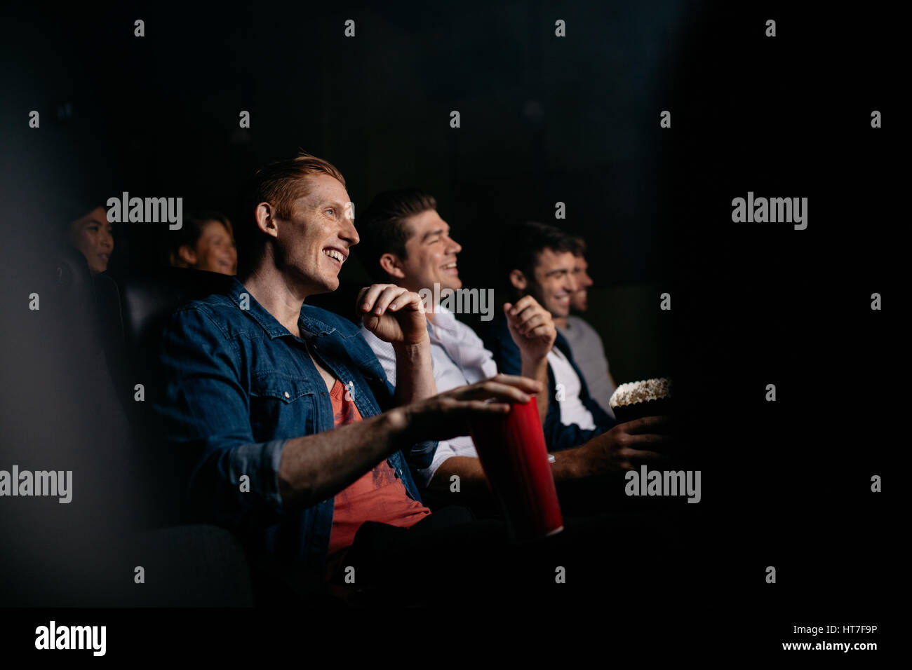 Sorridente giovane con gli amici nella sala cinema guardare film. Gruppo di persone che guardano film in teatro. Foto Stock