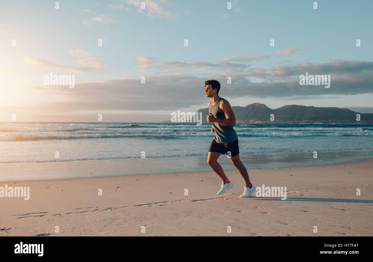 Montare il giovane uomo jogging sulla spiaggia. Sani di sesso maschile di lavoro in esecuzione nella mattina lungo la riva del mare. Foto Stock