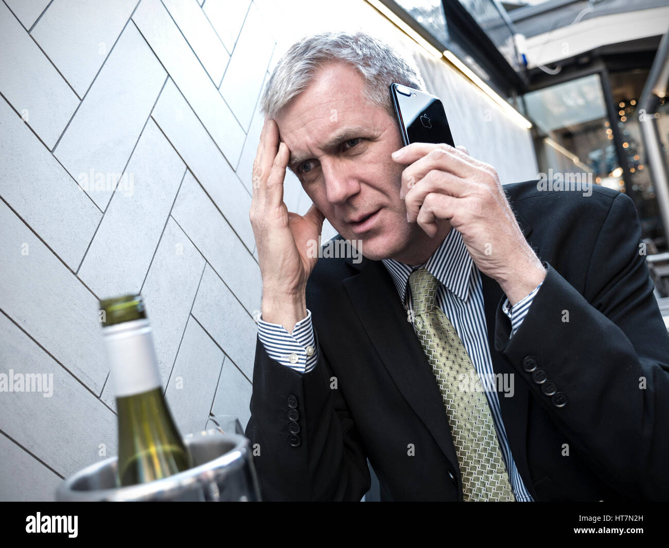 Imprenditore cattive notizie stressato e preoccupato per il suo iPhone 7 smartphone a alfresco café ristorante tavolo con bottiglia di vino in primo piano Foto Stock