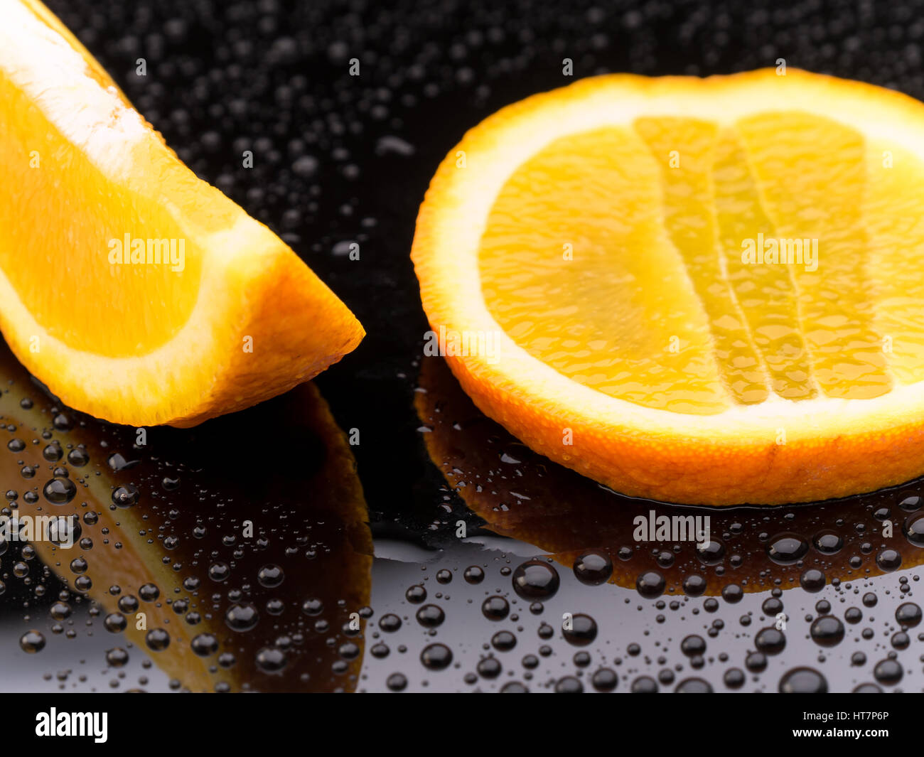 Arancione Sano frutta in pezzi su un nero superficie riflettente con goccioline di acqua Foto Stock