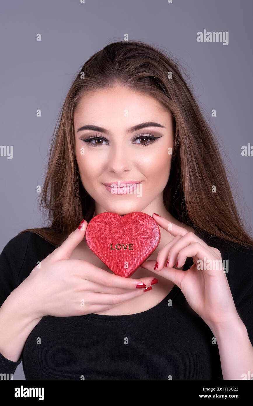 Giovane donna in possesso di una forma di cuore scatola di cioccolatini con incisa la parola amore. Foto Stock