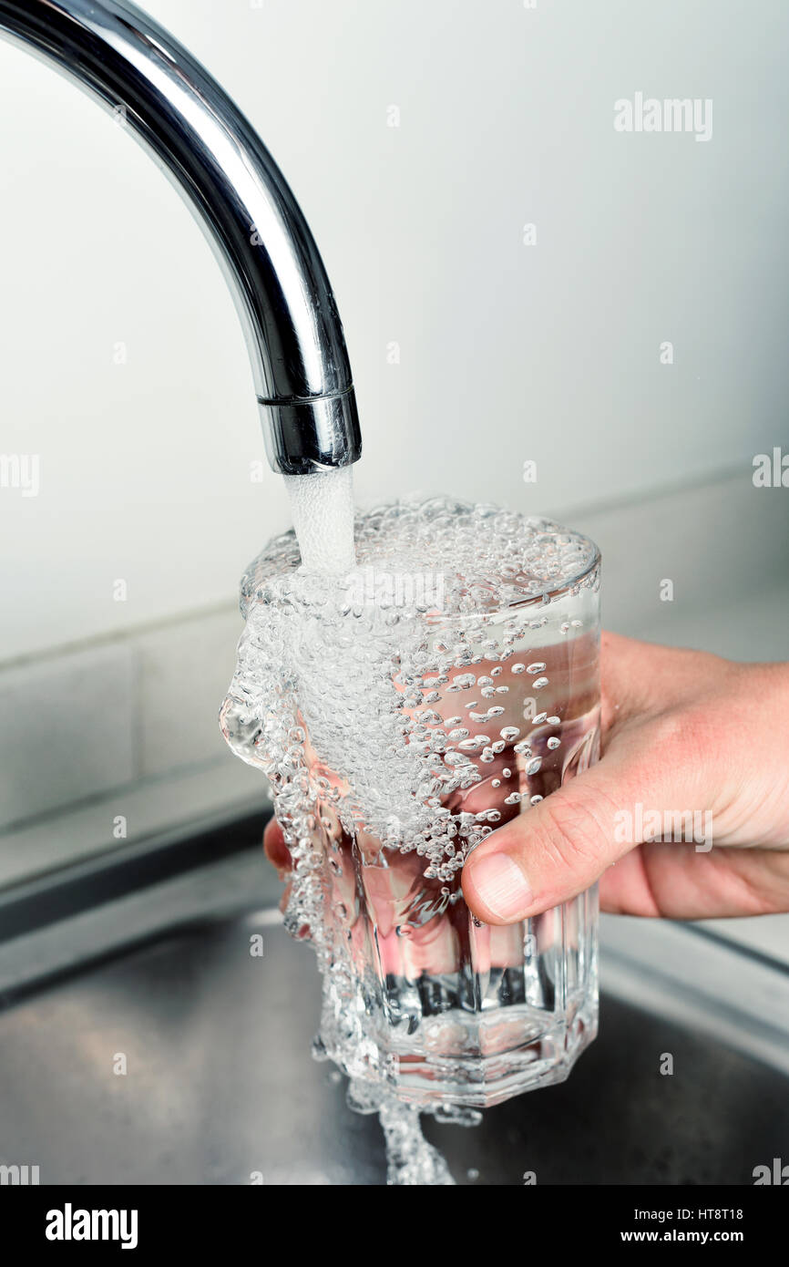 Primo piano di un giovane uomo caucasico riempire un bicchiere di acqua di rubinetto Foto Stock