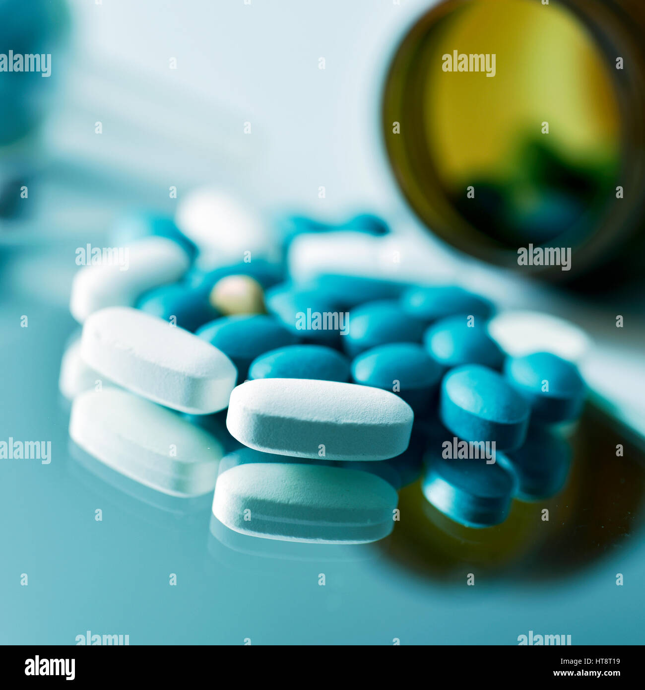 Primo piano di molte diverse pillole su una superficie riflettente e una bottiglia marrone con le pillole in background Foto Stock