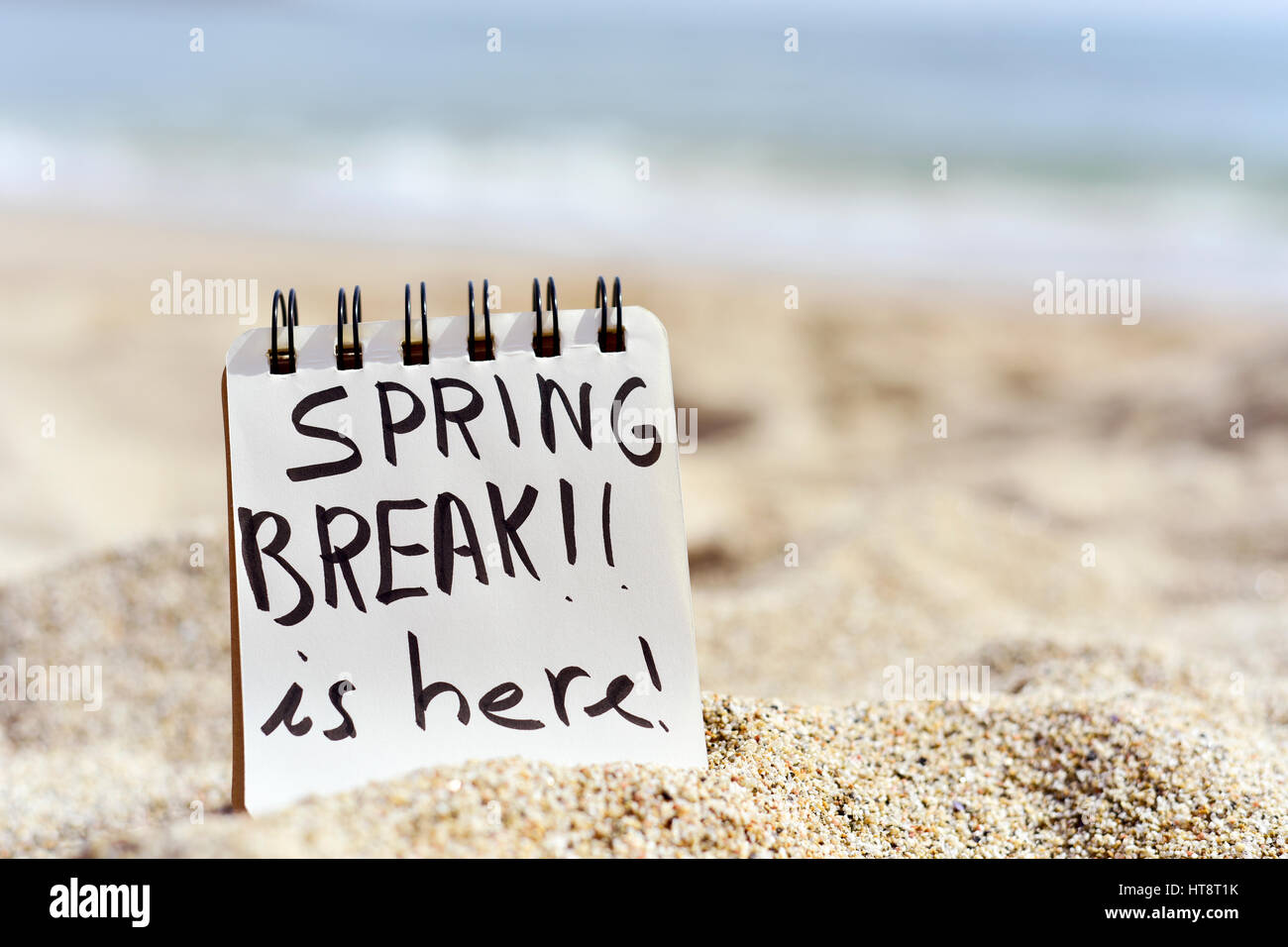Vista dettagliata di un blocco note con il testo spring break è qui scritto in esso, sulla sabbia di una spiaggia Foto Stock