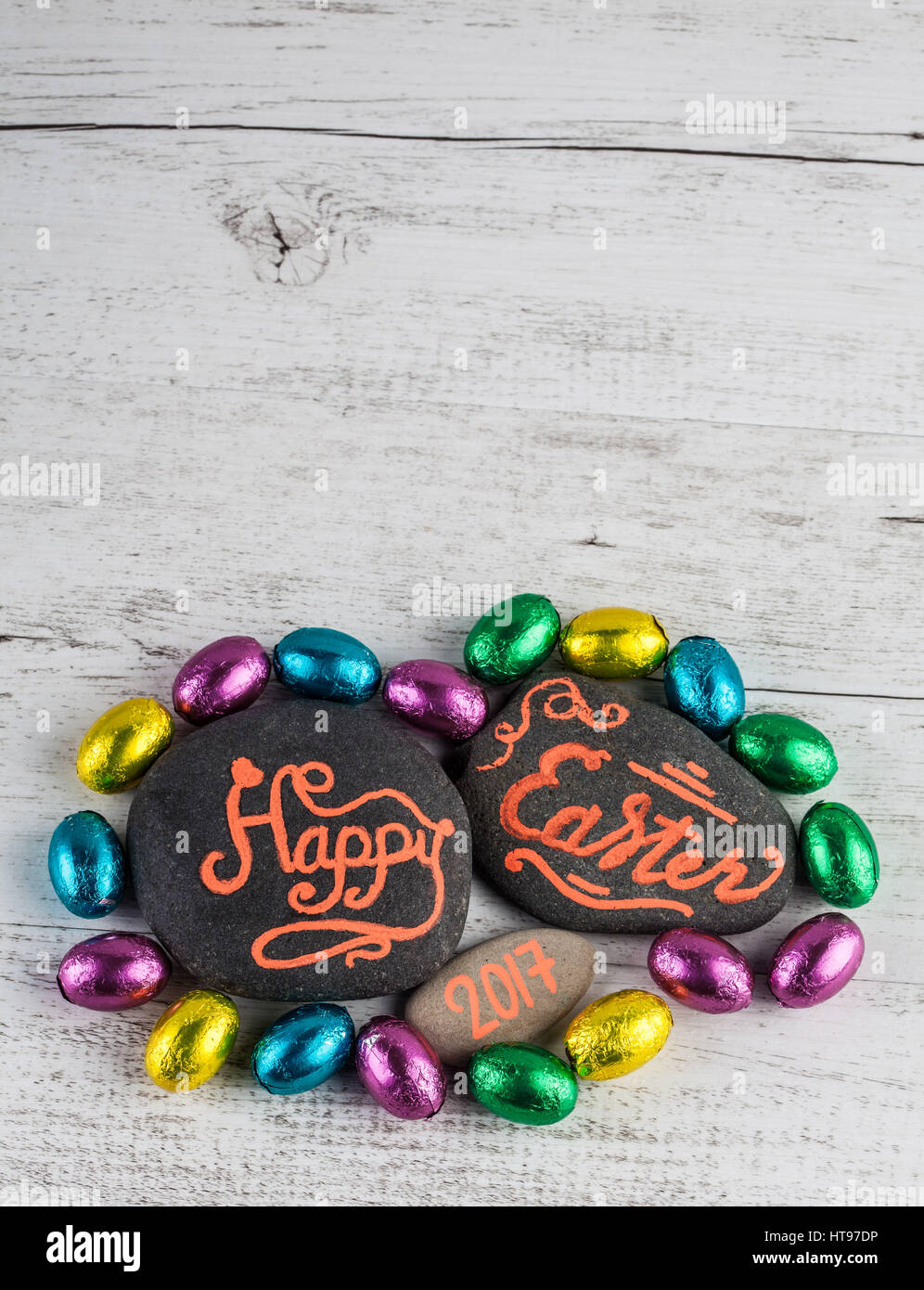 Felice Pasqua 2017 caratteri scritti su ciottoli con uova di cioccolato avvolto in foglio colorato. L'immagine verticale con spazio di copia Foto Stock