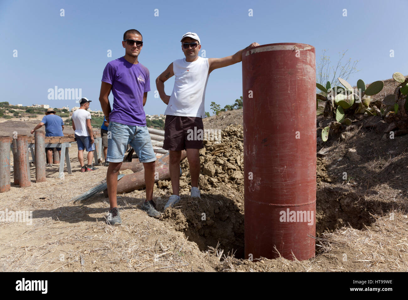 Due pyrotechnicians Maltese posano con il più grande tubo di lancio presso il sito di lancio di un professionista di spettacolo di fuochi d'artificio. impostato per una città Feste di Malta. Foto Stock