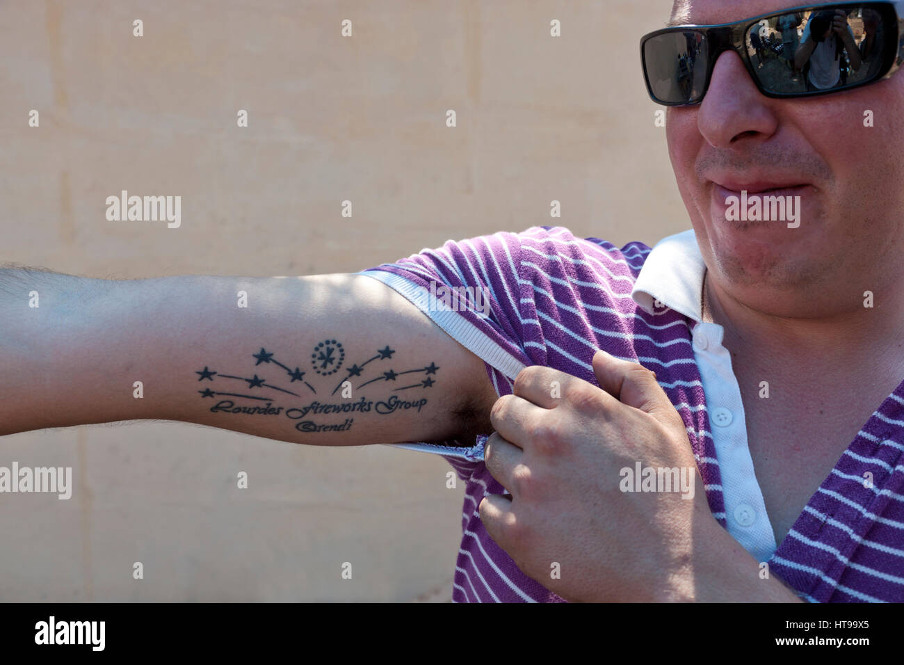Un pyrtechnician Maltese si mette in mostra il tatuaggio con il logo della fabbrica di fuochi d'artificio che egli fa parte del. Foto Stock