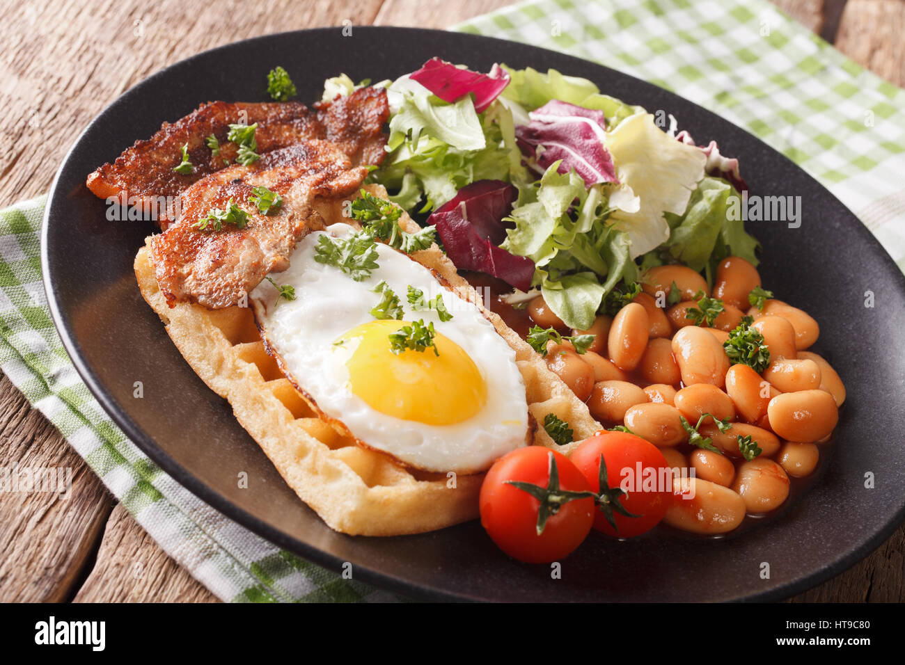 La prima colazione con uovo fritto, waffle, pancetta, mescolare la lattuga e fagioli vicino sul tavolo orizzontale. Foto Stock
