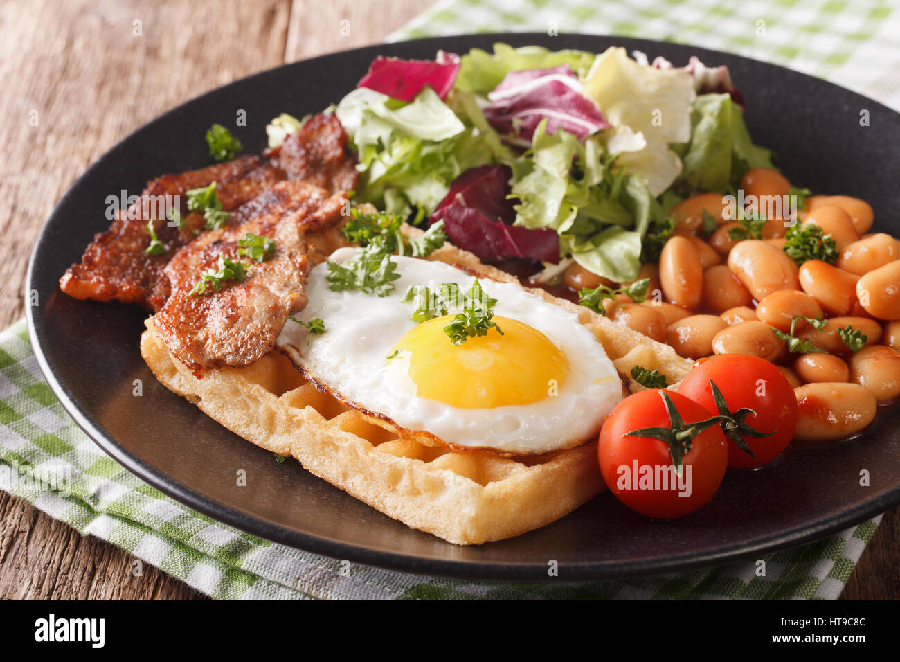 Prima colazione Inglese con uovo fritto, cialde, pancetta, insalata di fagioli e vicino sul tavolo orizzontale. Foto Stock