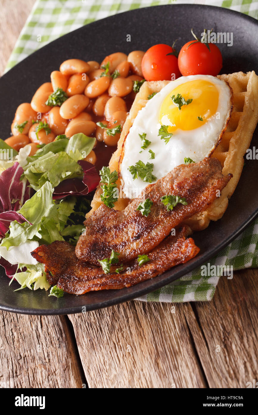 La deliziosa prima colazione: uovo fritto, cialde, pancetta, fagioli e insalata di close-up su una piastra. In verticale Foto Stock