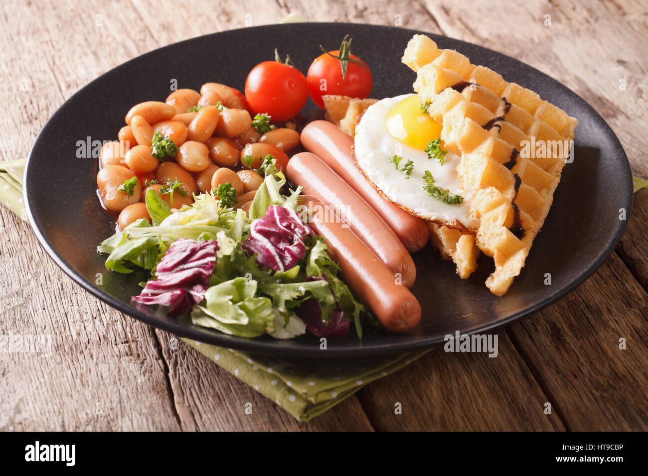 Frittelle fritte con uova, salsicce, fagioli e insalata fresca close-up su una piastra orizzontale. Foto Stock