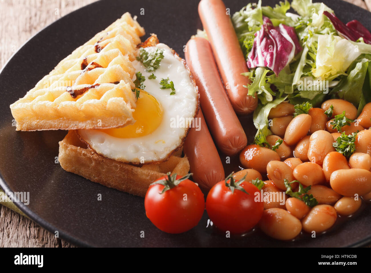 La deliziosa prima colazione: uovo fritto, cialde, salsicce, fagioli e insalata di close-up su una piastra orizzontale. Foto Stock