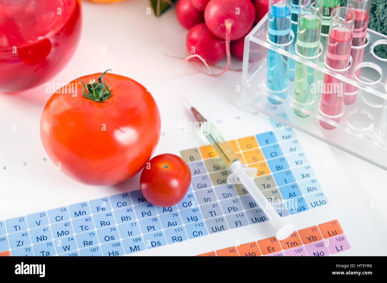 Pomodori, siringa, tubi di test in laboratorio su tavola periodica. Alimenti geneticamente modificati concezione. Foto Stock