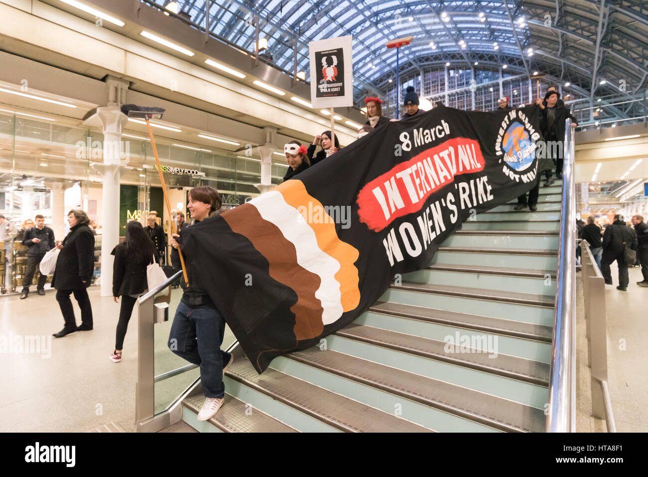 Londra, Regno Unito. 8 marzo 2017. Londra femministe polacche sono state unite da Sciopero Globale delle Donne, l'in solidarietà con le donne in 46 paesi prendono parte Internazionale delle Donne Sciopero sulla Giornata internazionale della donna per celebrare le lotte delle donne di tutto il mondo in un flash mob a St Pancras International. Vestita di nero e rosso abbigliamento, dopo aver professato la loro routine con ombrelloni con messaggi su di essi e un grande banner in ingresso alla stazione ferroviaria internazionale di St Pancras sono scese all'atrio principale per eseguire. Credito: Peter Marshall / Alamy Live News Foto Stock
