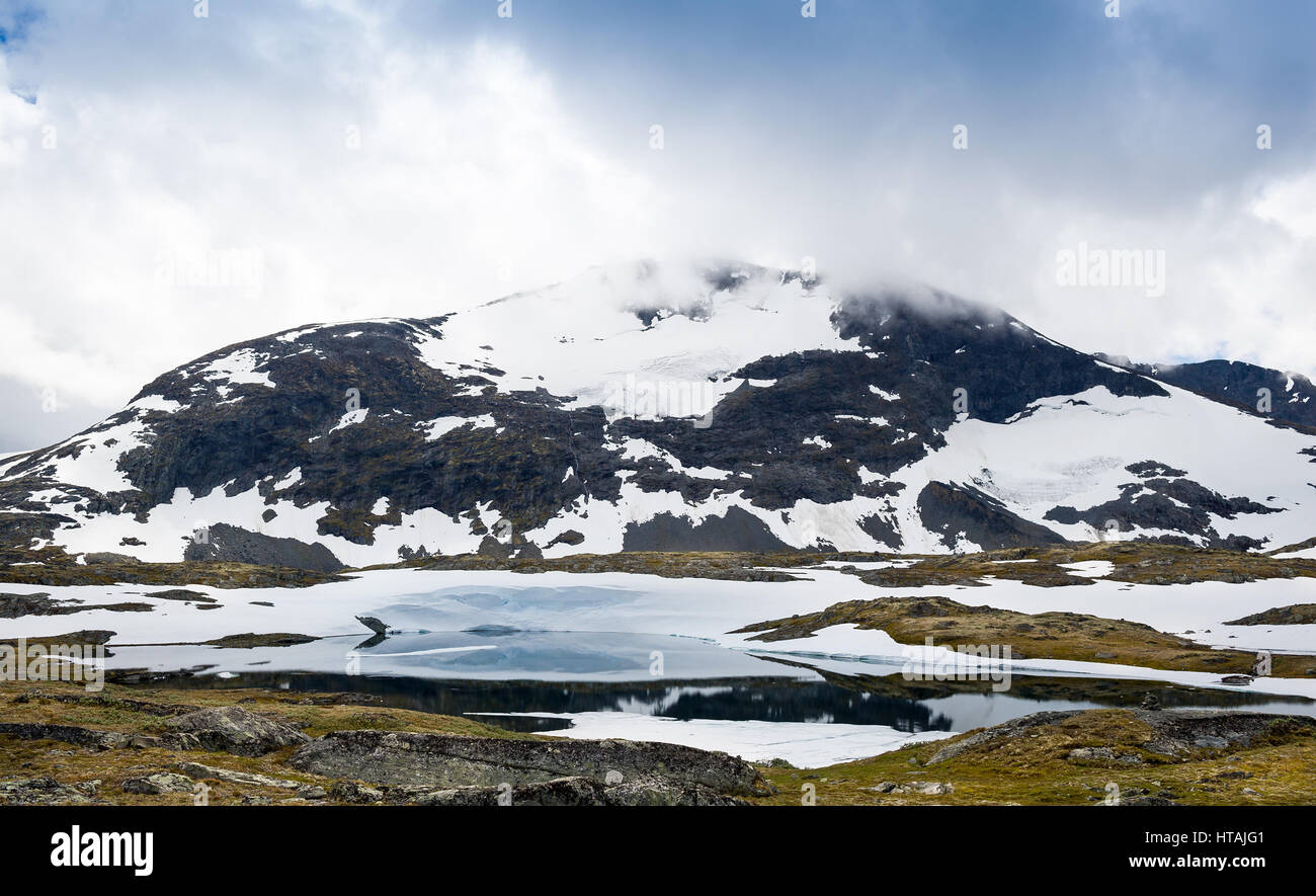 Vista della montagna rocciosa con la neve sul pendio e piccolo stagno sotto la montagna. Strada 55, Sognefjellet, Norvegia. Foto Stock
