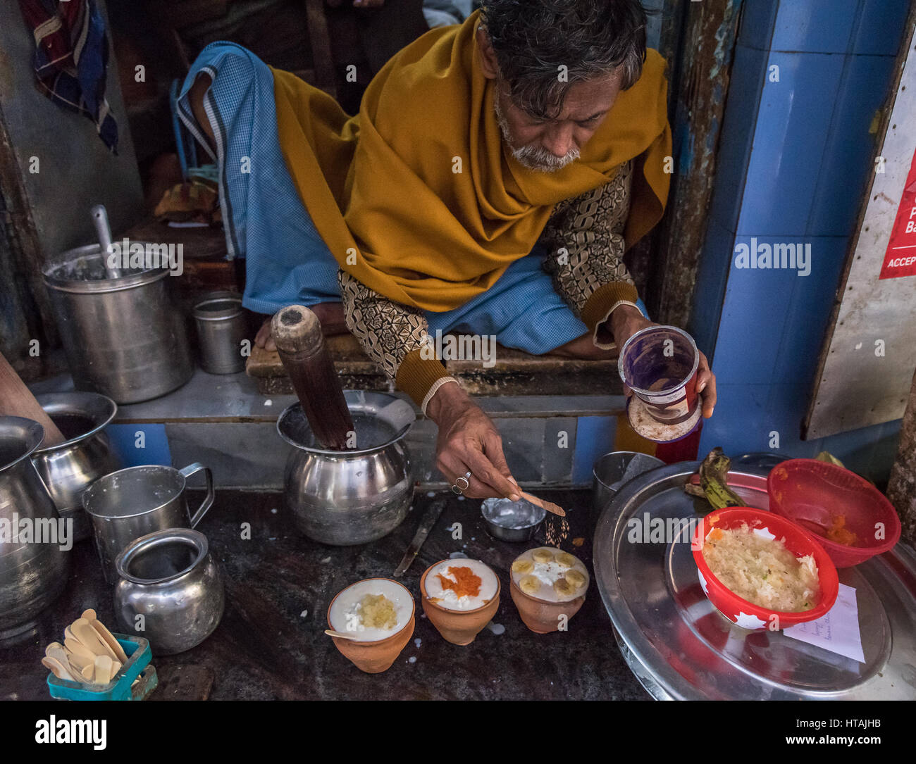 Proprietario del Blue Lassi perpares suo yogurt da bere davanti al suo negozio di Varanasi (India). Foto Stock