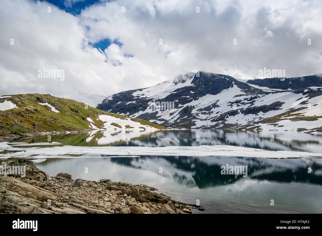 Verdi colline, rocce innevate e lago di montagna - paesaggi panoramici della famosa strada innevata 55, Lom, Norvegia. Foto Stock