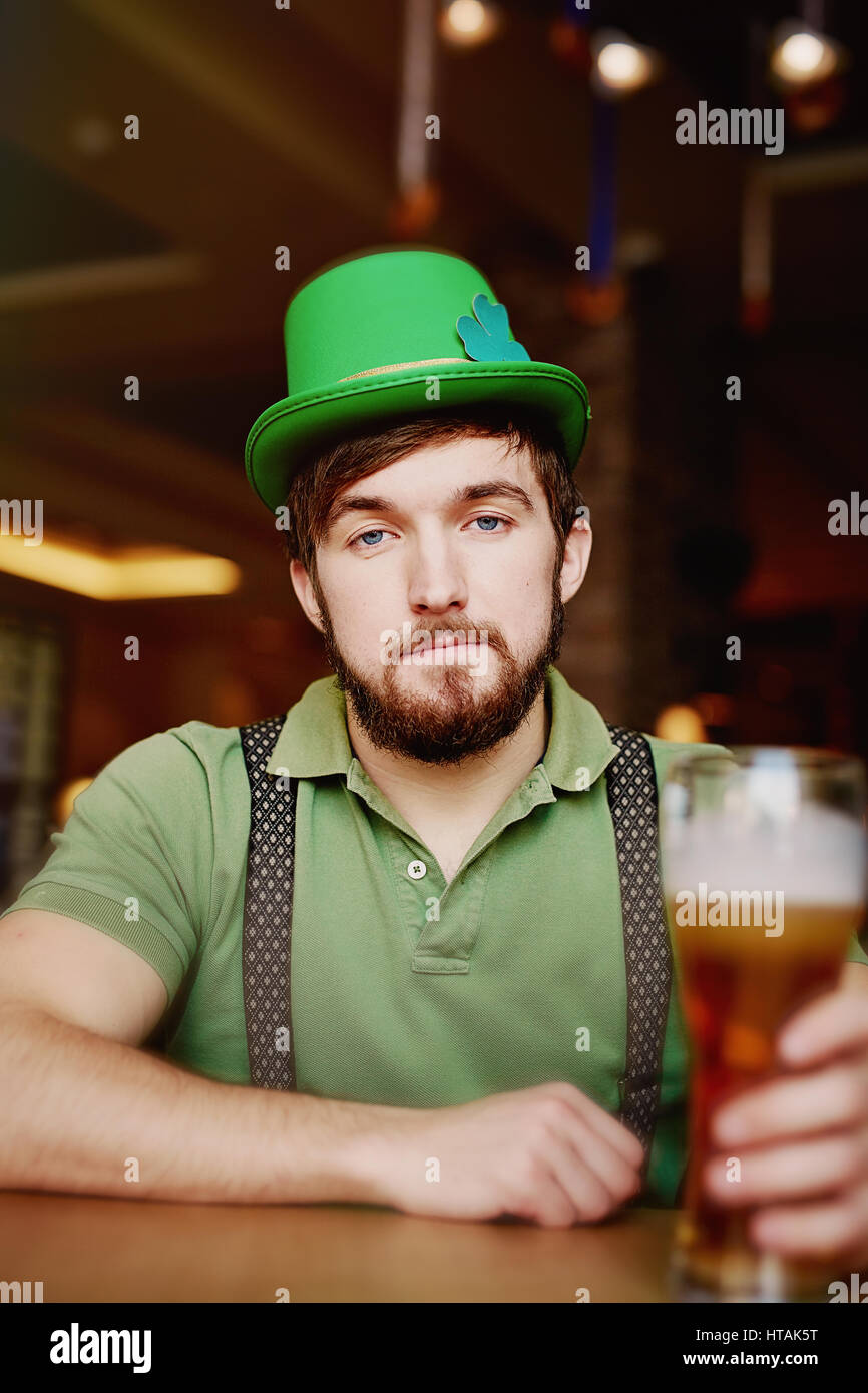 Ritratto di uomo barbuto in leprechaun costume, con green Bowler cappello e il patibolo, seduti al banco bar con bicchiere di birra chiara nel classico Iris Foto Stock