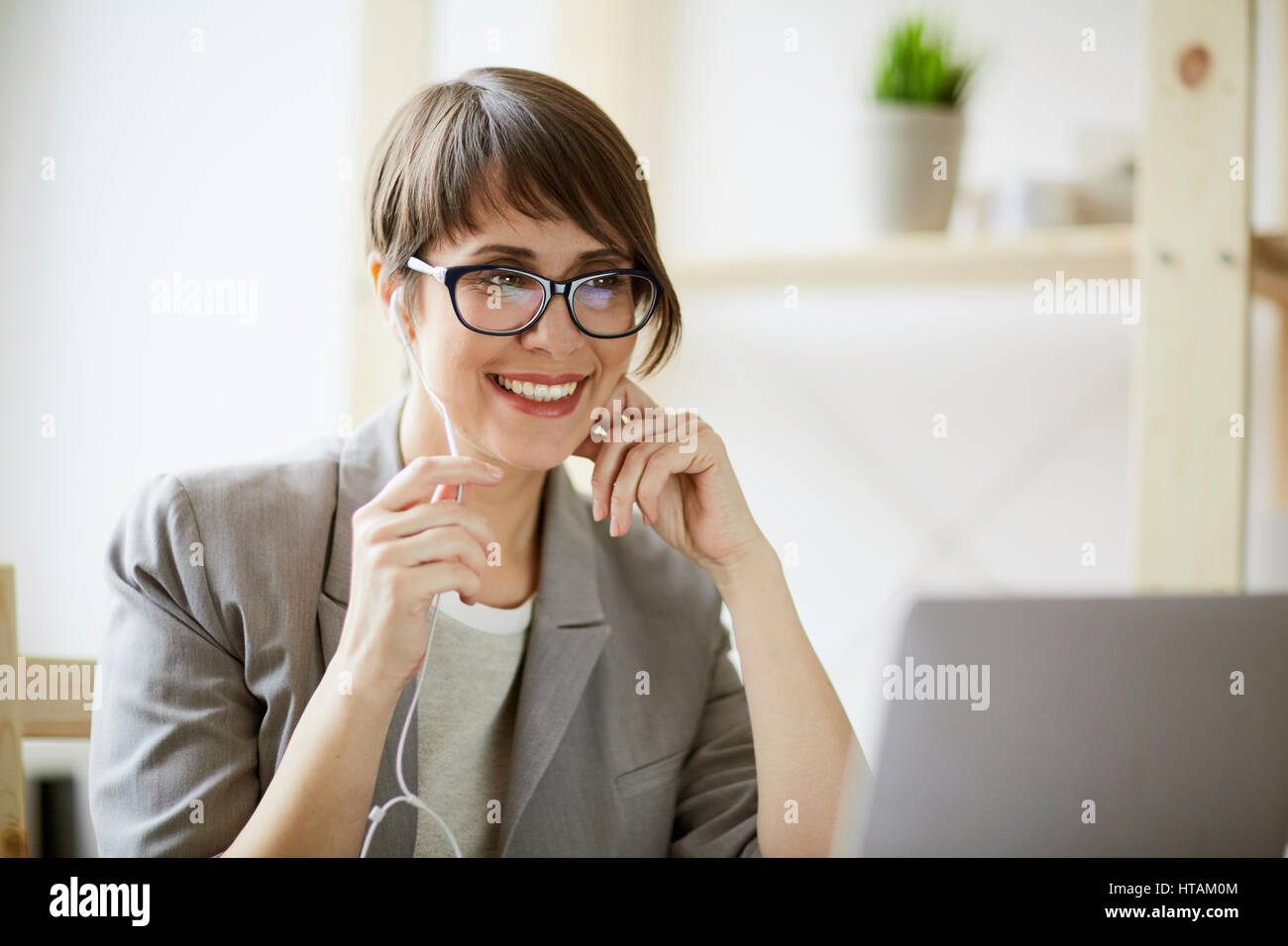 Ritratto di giovane imprenditrice di successo che indossa creative taglio di capelli e bicchieri sorridendo allegramente mentre si tiene la videochat usando le mani libere mic e la Foto Stock