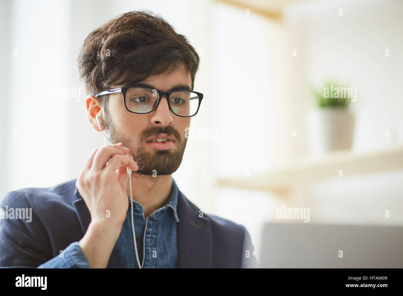 Ritratto di giovane uomo creativo che indossano occhiali focalizzata tenendo la videochat intervista di applicare per il lavoro in posizione utilizzando il vivavoce e microfono portatile a Foto Stock