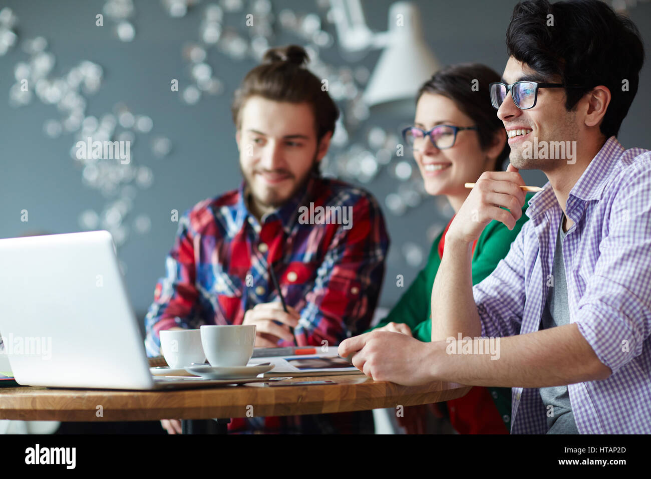 Vista laterale di un gruppo di giovani creativi di indossare abiti casual collaborando alla riunione in ufficio e sorridente guardando lo schermo del notebook Foto Stock