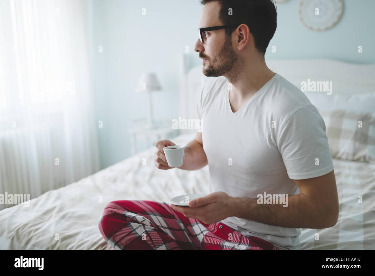 Uomo in pigiama godendo il caffè al mattino in camera da letto Foto Stock