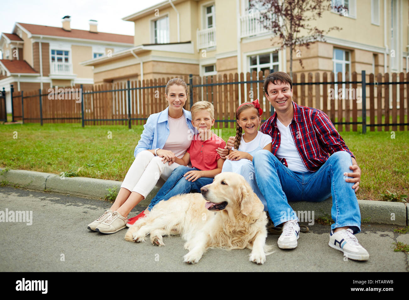 Ritratto di famiglia felice con due figli, un ragazzo e una ragazza, e loro golden retriever cane seduto fuori sul verde prato di fronte al loro nuovo grande Foto Stock