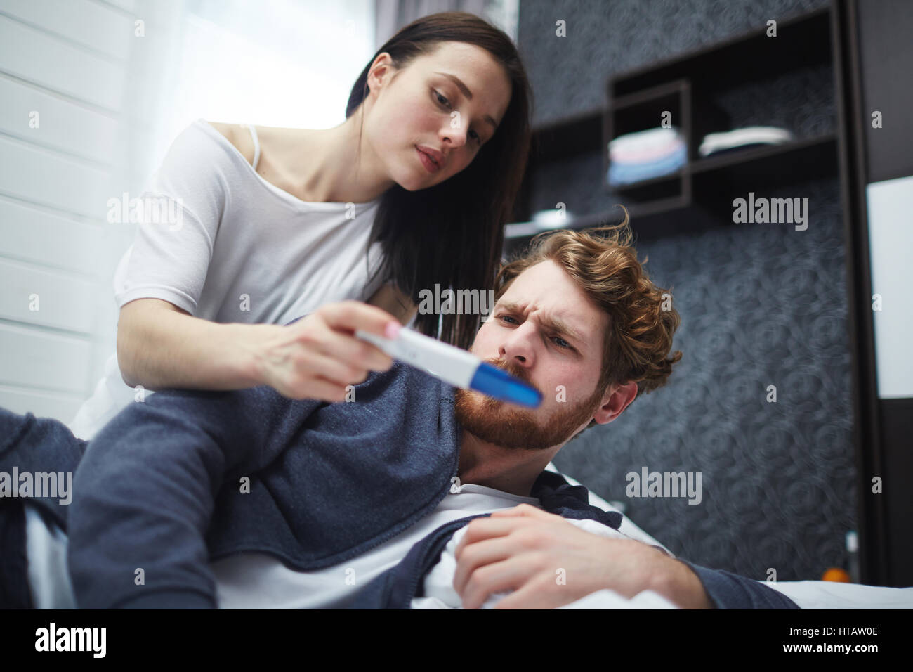 Scettico uomo faccia triste mentre la moglie che mostra lui test di gravidanza Foto Stock
